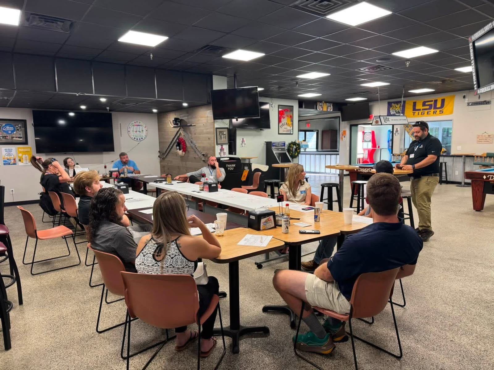 Wide view of a meeting room with people listening from both sides of the tables as a person presents